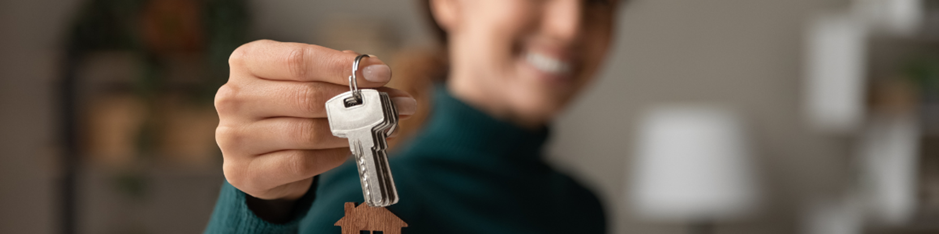 Northern Ireland based female landlord holds out house keys to new tenant with small wooden keyring in the shape of a house attached
