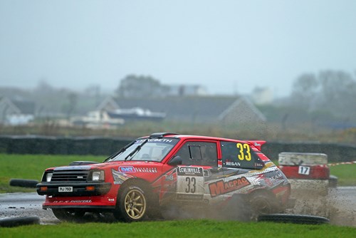 Red and white retro rally car skids in mud as part of NI rally championship